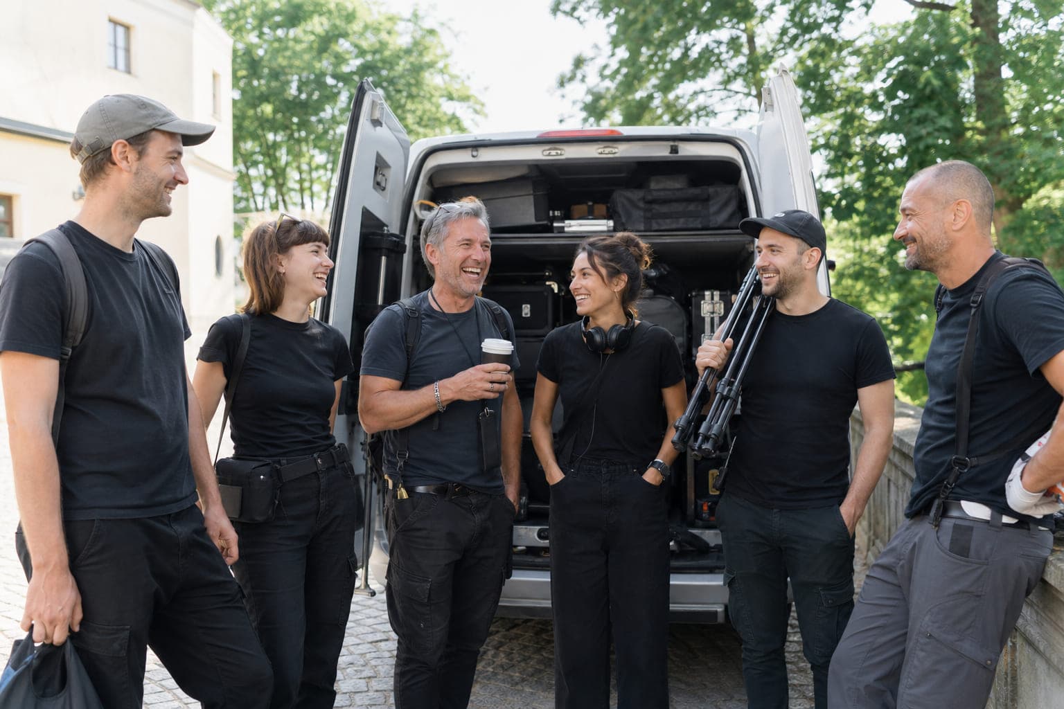 Ein Filmteam steht lachend vor einem Transporter mit Kamerakoffern.