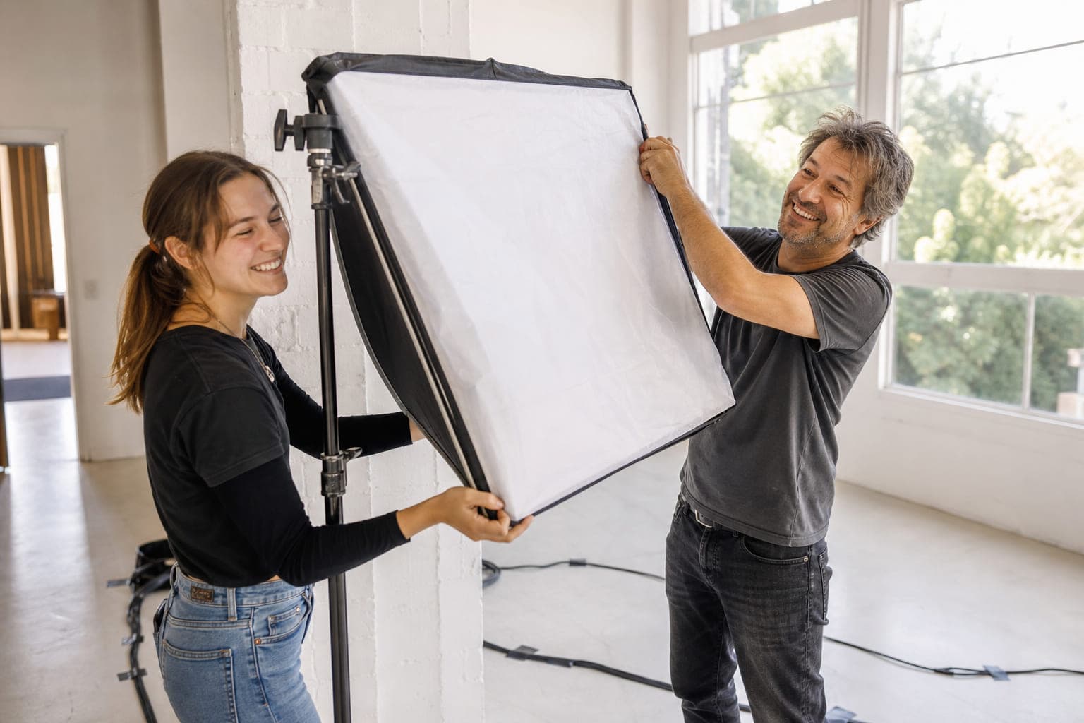 Zwei Crewmitglieder bauen lachend eine große Softbox in einem hellen Raum auf.
